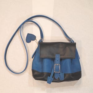 May include: A blue and black leather crossbody bag with a flap closure and adjustable strap. The bag features a silver buckle and a heart-shaped tag. The bag is approximately 8 inches wide and 9 inches tall.