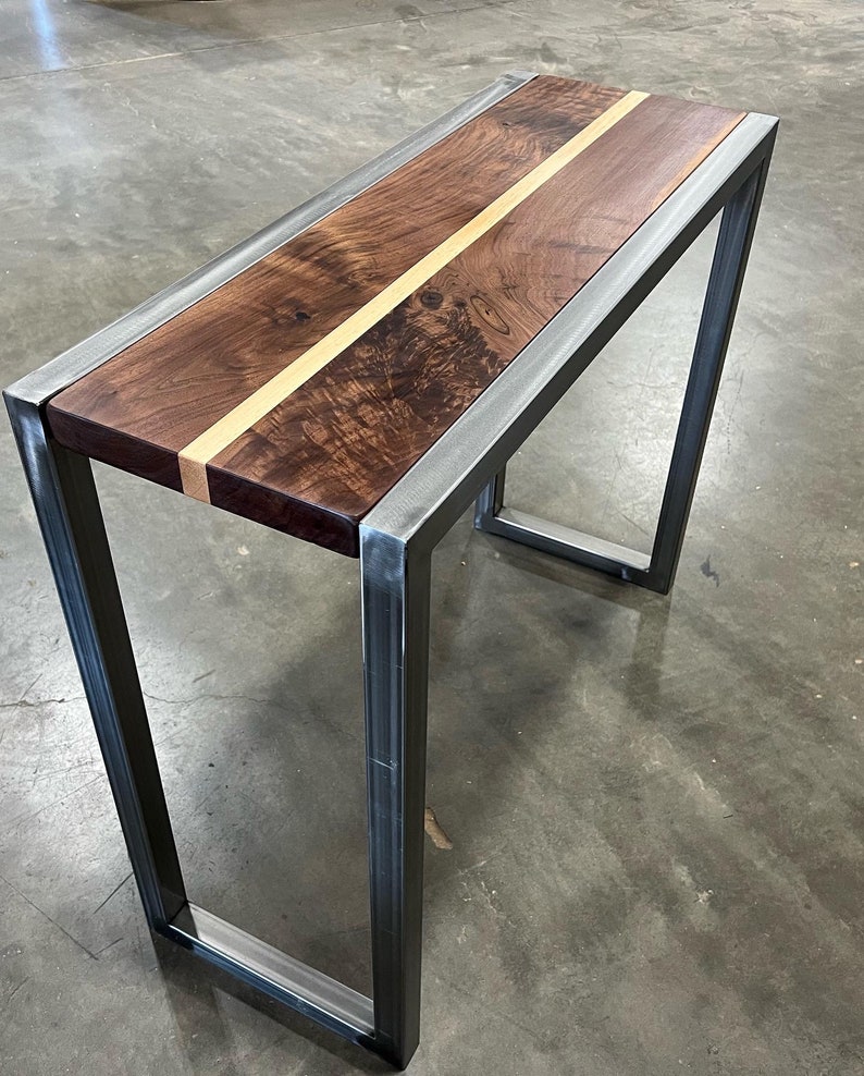 Pu&ograve; includere: Un moderno tavolino consolle con piano in legno scuro con una striscia di legno chiaro al centro. Il piano &egrave; incorniciato da un bordo in metallo argentato e sostenuto da gambe in metallo argentato.