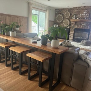 May include: A long wooden table with black metal legs and four matching stools. The table is placed in a living room with a fireplace and a couch.