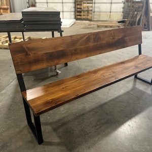 May include: A rustic wooden bench with a black metal frame. The bench has a wide, flat seat and a tall backrest. The wood has a natural, distressed finish.