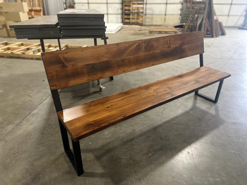 May include: A rustic wooden bench with a black metal frame. The bench has a wide, flat seat and a tall backrest. The wood has a natural, distressed finish.