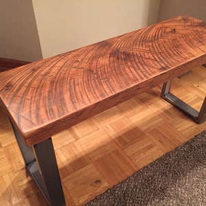 May include: A wooden bench with a natural wood finish and a metal frame. The bench has a rustic look and is made of reclaimed wood.