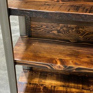 May include: A rustic wooden shelf unit with three shelves. The shelves are made of stained wood with visible grain patterns and knots. The wood has a warm, brown tone with darker accents. The frame is made of gray metal.