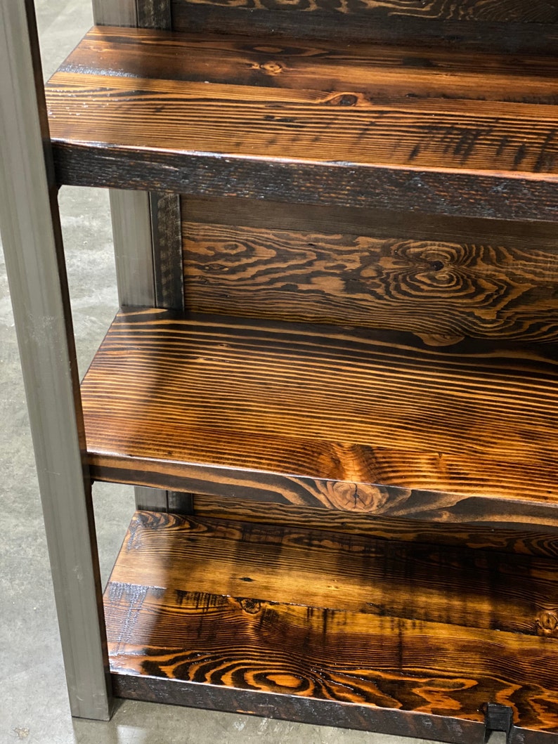 May include: A rustic wooden shelf unit with three shelves. The shelves are made of stained wood with visible grain patterns and knots. The wood has a warm, brown tone with darker accents. The frame is made of gray metal.