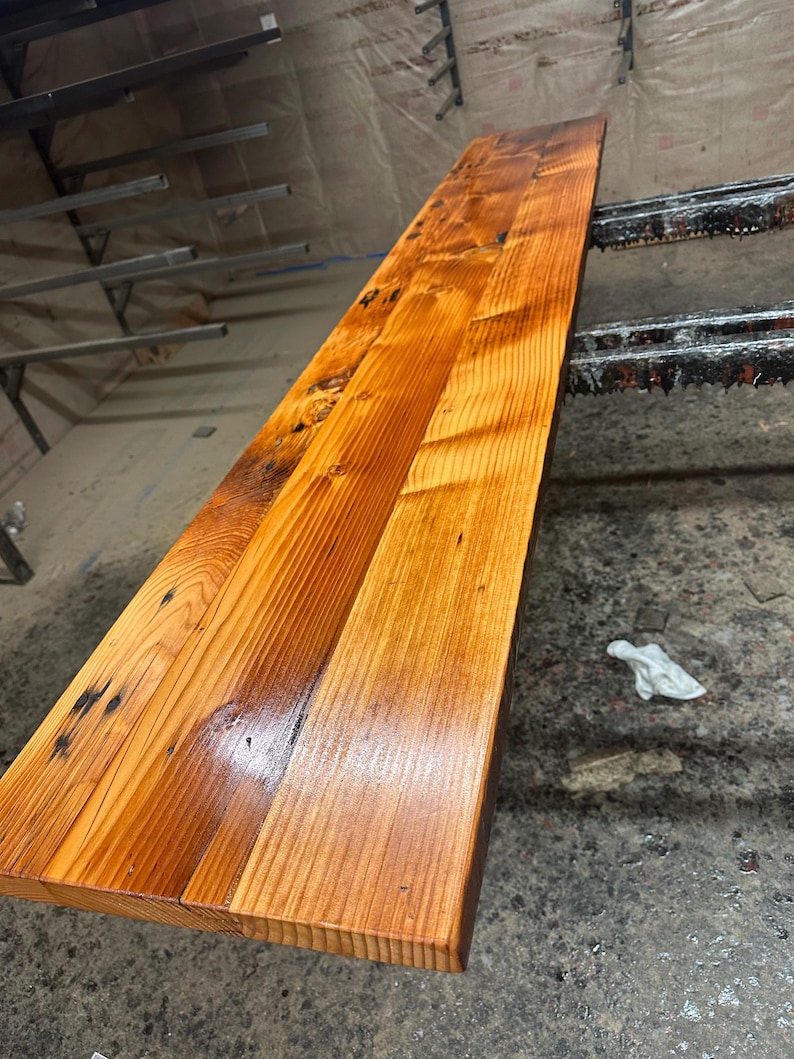 May include: A long, narrow wooden countertop made of reclaimed wood planks. The wood has a natural, rustic finish with knots and grain patterns. The countertop is stained a rich amber color and has a glossy finish.