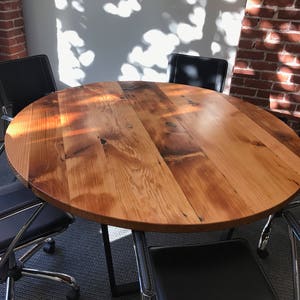 May include: A round wooden table with a natural wood finish and black metal legs. The table is surrounded by four black leather chairs with chrome bases.