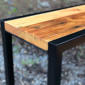 May include: A wooden table top with a black metal frame. The table top is made of reclaimed wood with a natural finish. The metal frame is painted black.