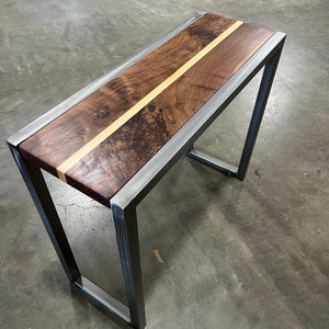 May include: A rectangular bench with a dark wood top featuring a light wood stripe down the center. The wood is framed by a silver metal border and supported by a matching metal frame. The bench is approximately 48 inches long.