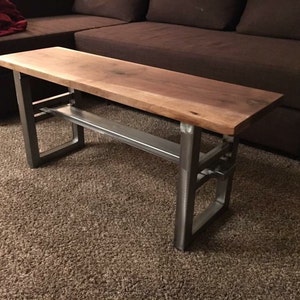 May include: A wooden table with a live edge top and a metal frame. The table has a shelf underneath the top. The table is sitting on a brown carpet.