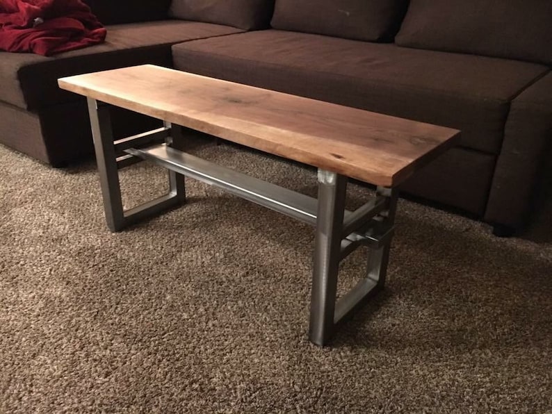 May include: A wooden table with a live edge top and a metal frame. The table has a shelf underneath the top. The table is sitting on a brown carpet.