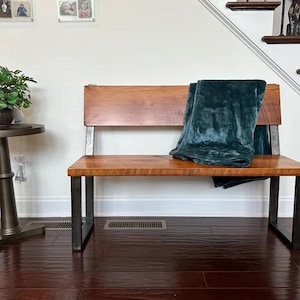 May include: A wooden bench with a teal blanket on top. The bench has a metal frame and a wooden seat and back.