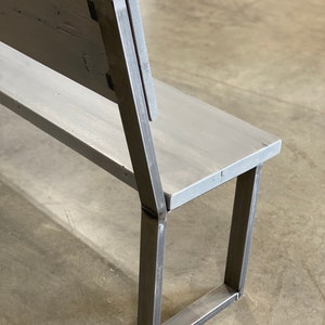 May include: A gray wooden bench with a metal frame. The bench has a back and a seat. The metal frame is made of square tubing. The bench is sitting on a concrete floor.