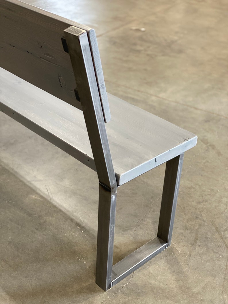 May include: A gray wooden bench with a metal frame. The bench has a back and a seat. The metal frame is made of square tubing. The bench is sitting on a concrete floor.