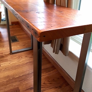 May include: A rustic wooden table top with a natural wood finish sits on a metal frame with a black powder coat finish. The table is narrow and has a rectangular shape.