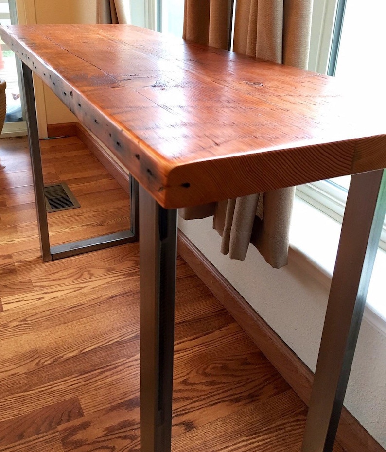 May include: A rustic wooden table top with a natural wood finish sits on a metal frame with a black powder coat finish. The table is narrow and has a rectangular shape.