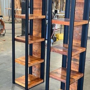 May include: Two rustic wooden shelves with a black metal frame. The shelves are made of reclaimed wood with a natural finish. The metal frame is a dark color. The shelves are designed to be freestanding and are suitable for displaying items.