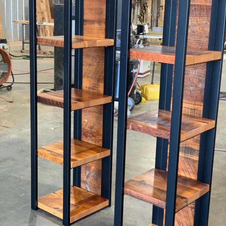 May include: Two rustic wooden shelves with a black metal frame. The shelves are made of reclaimed wood with a natural finish. The metal frame is a dark color. The shelves are designed to be freestanding and are suitable for displaying items.