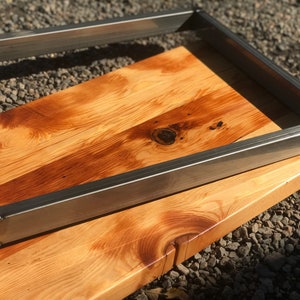 May include: A wooden tabletop with a metal frame. The wood is a light brown color with a reddish hue. The metal frame is silver and has a rectangular shape.