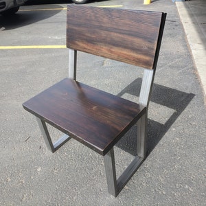 May include: A dark brown wooden chair with a metal frame. The chair has a high back and a wide seat. The chair is made of reclaimed wood and metal.