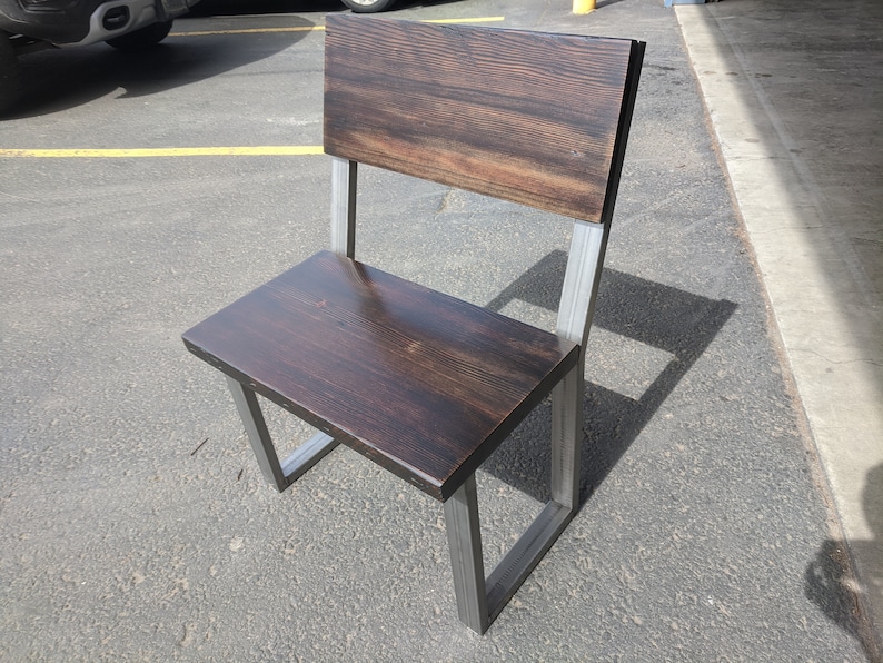 May include: A dark brown wooden chair with a metal frame. The chair has a high back and a wide seat. The chair is made of reclaimed wood and metal.