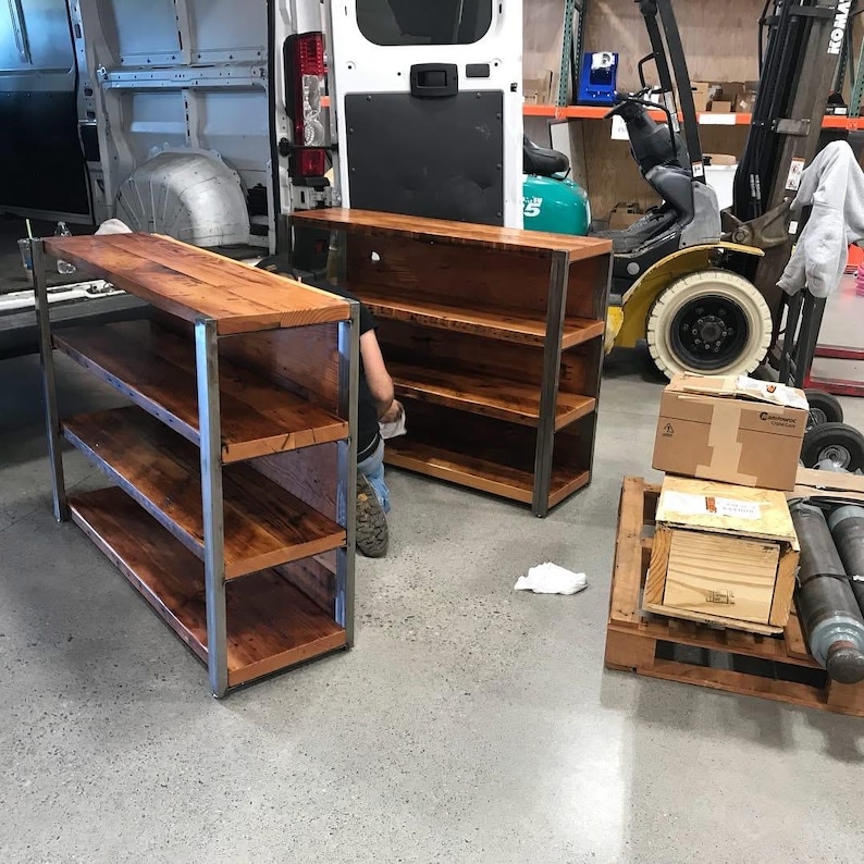 May include: Two wooden shelves with a metal frame. The shelves are made of stained wood and have a natural grain. The metal frame is silver. The shelves are in a warehouse setting.