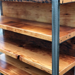 May include: A rustic wooden bookshelf with four shelves. The shelves are made of light-colored wood with a natural finish, and the frame is made of dark metal. The shelves are supported by vertical metal bars.