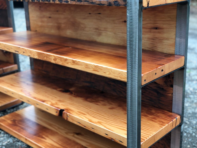 May include: A rustic wooden bookshelf with four shelves. The shelves are made of light-colored wood with a natural finish, and the frame is made of dark metal. The shelves are supported by vertical metal bars.