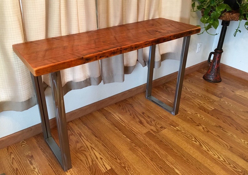 May include: A rustic wooden table top with a natural wood finish sits on a metal frame with a black powder coat finish. The table is in a room with hardwood floors.