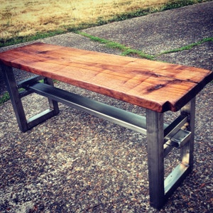 May include: A wooden bench with a metal frame. The bench has a natural wood finish and the frame is made of silver metal. The bench is sitting on a concrete surface.