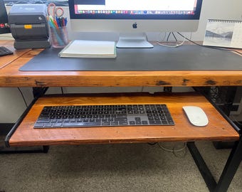 May include: A wooden desk with a black keyboard and a white mouse on a pull-out shelf. The desk has a black surface and a wooden frame.