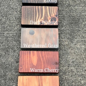 May include: Five wood samples stained in different colors: Ebony, Dark Walnut, Weathered Gray, Warm Cherry, and Natural.