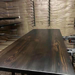 May include: A dark brown wooden table top with a natural wood grain pattern. The table top is smooth and polished, with a black edge.