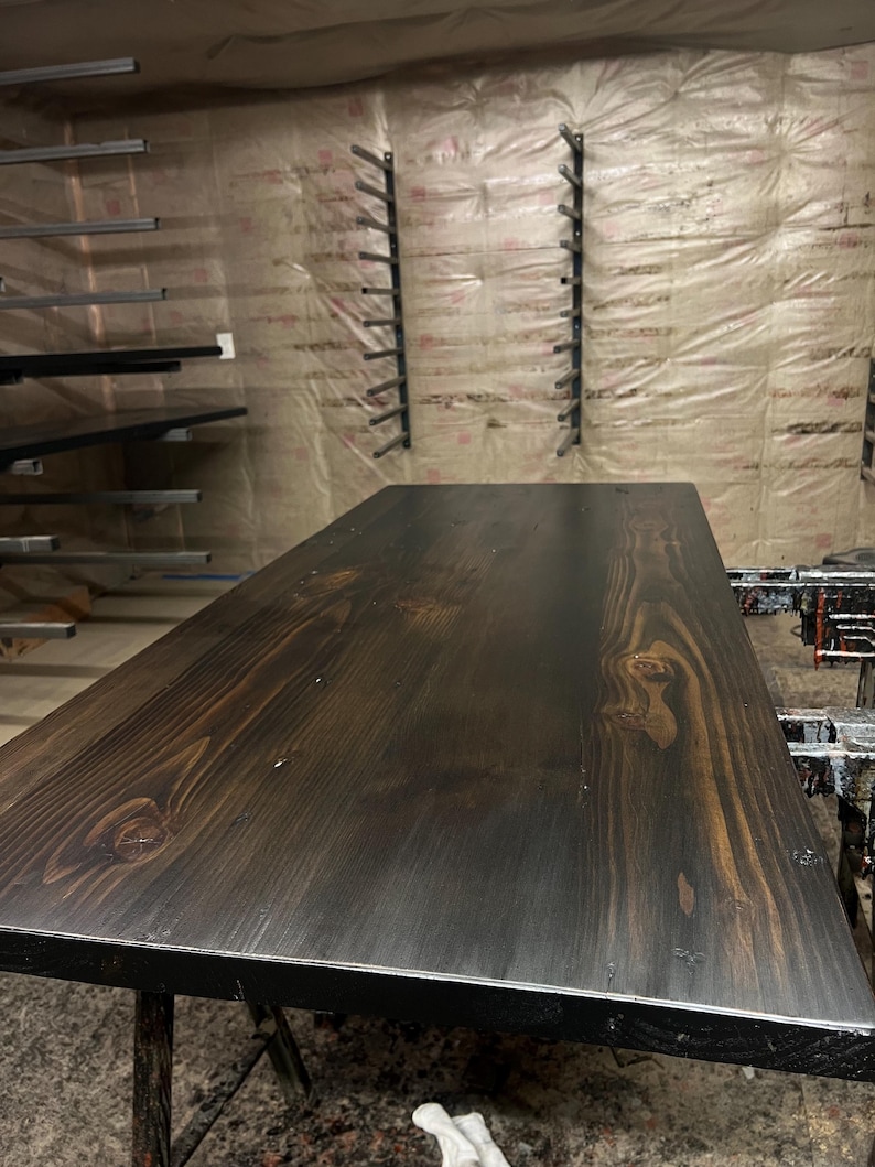 May include: A dark brown wooden table top with a natural wood grain pattern. The table top is smooth and polished, with a black edge.