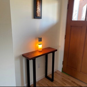 May include: A wooden table with black metal legs and a white and black striped lamp on top. The table is in a room with a wooden door and white walls.