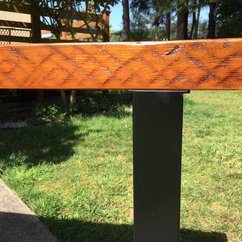 May include: Close-up of a wooden railing with a black metal support post. The wood has a natural grain and is stained a rich brown color.
