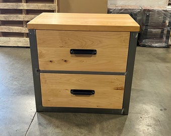 May include: Two-drawer wooden nightstand with a metal frame. The drawers have black metal handles and the wood is a light natural color.