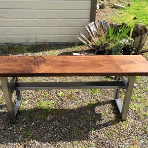 May include: A wooden bench with a dark brown top and a metal frame. The bench has a shelf underneath the top.