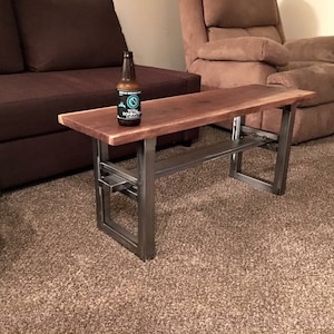 May include: A dark brown wooden coffee table with a metal frame. The table has a shelf underneath and is sitting on a brown carpet.