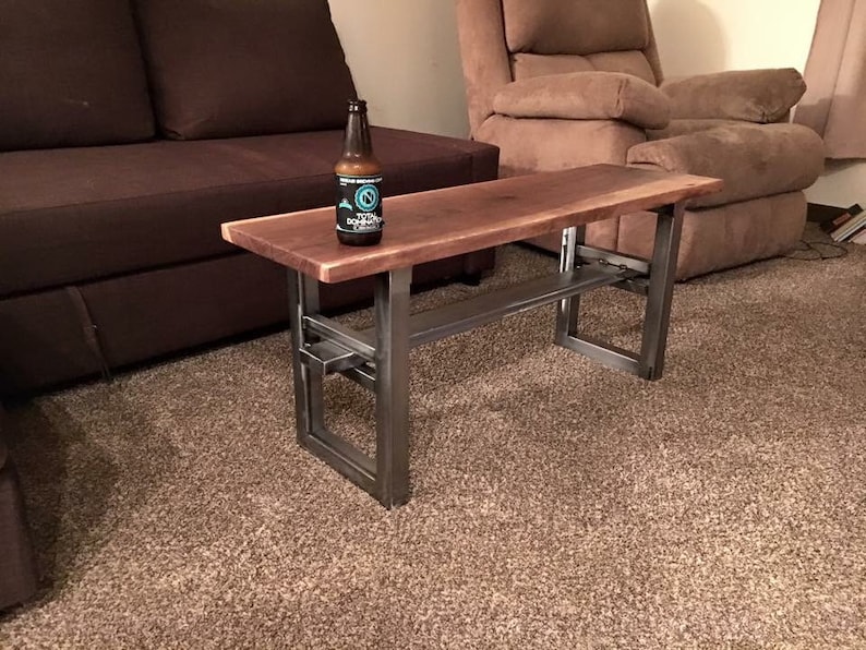 May include: A dark brown wooden coffee table with a metal frame. The table has a shelf underneath and is sitting on a brown carpet.