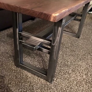 May include: A wooden coffee table with a live edge top and a metal frame. The frame has a geometric design with a shelf underneath the top.
