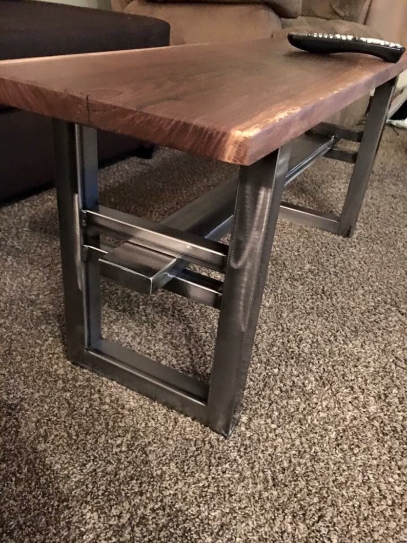 May include: A wooden coffee table with a live edge top and a metal frame. The frame has a geometric design with a shelf underneath the top.