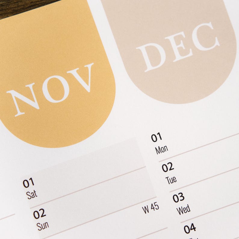 Puede incluir: Primer plano de una p&aacute;gina de calendario con los meses de noviembre y diciembre. La palabra "NOV" est&aacute; en blanco sobre un fondo amarillo-naranja, y "DEC" est&aacute; en blanco sobre un fondo beige claro. El calendario muestra las fechas y los d&iacute;as de la semana.