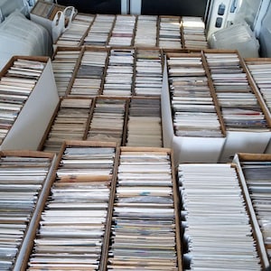 Puede incluir: Una colección de artículos vintage, posiblemente cromos o postales, cuidadosamente organizados en cajas de cartón. Las cajas están dentro de un vehículo, lo que sugiere una exhibición o almacenamiento móvil. Los artículos están apilados en filas.