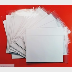 Op de afbeelding: Een waaier van witte enveloppen in transparante plastic hoezen tegen een rode achtergrond. De enveloppen zijn rechthoekig en lijken standaard van formaat te zijn. De transparante hoezen laten het wit van de enveloppen opvallen.