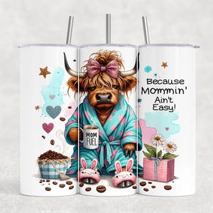 A funny Highland cow in a polka-dot robe, pink bunny slippers, and coquette bow holding a "Mom Fuel" mug, surrounded by coffee beans, glitter hearts, daisies, and a pink gift box. Text reads, "Because Mommin’ Ain’t Easy!" on a playful background.