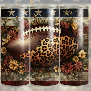 May include: A cylindrical tumbler decorated with a football design, incorporating a leopard print pattern, floral elements, and an American flag motif. The design includes stars, stripes, and a distressed wood effect.