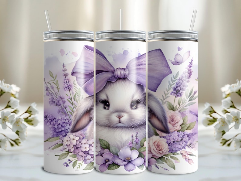 A beautiful 20 oz tumbler wrap featuring an adorable white Easter bunny with big, expressive eyes, wearing a large purple bow. Surrounded by soft pastel florals, lavender, and butterflies in a dreamy watercolor style on a white background