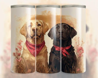 May include: A cylindrical tumbler featuring two Labrador Retrievers. One is golden, the other black, both wearing red bandanas and bows. The background has a watercolor effect with pink flowers and a beige backdrop.