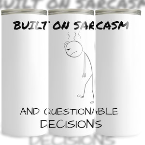 Może przedstawiać: Biały kubek z srebrną obwódką. Tekst "BUILT ON SARCASM" i "AND QUESTIONABLE DECISIONS" jest wydrukowany na czarno. Przedstawiona jest również postać ludzika z parą wydobywającą się z głowy.