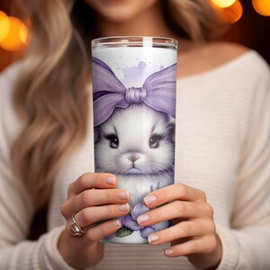 A beautiful 20 oz tumbler wrap featuring an adorable white Easter bunny with big, expressive eyes, wearing a large purple bow. Surrounded by soft pastel florals, lavender, and butterflies in a dreamy watercolor style on a white background